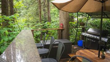 An outdoor dining area with a wooden table, metal chairs, a barbecue grill, and a canopy.