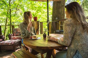 Two people sitting at a wooden table outdoors, with a wooden deck and chairs in the background.