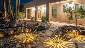 Un edificio moderno con un sendero de piedra, plantas de cactus e iluminación exterior.