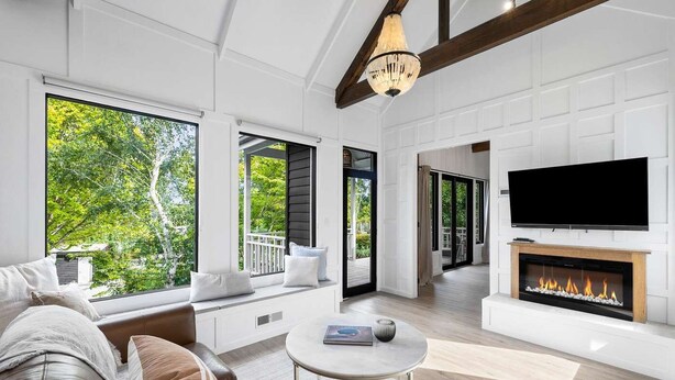 A modern living room with large windows, a fireplace, and a television.