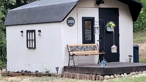A small, single-story building with a black door and a bench outside. - Inn the Woods - cozy place in the Smokies (Sevierville)