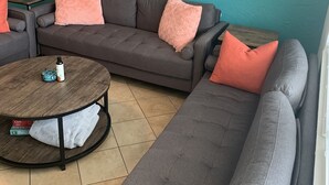Een woonkamer met een grijze hoekbank, een klein rond tafeltje en twee decoratieve wanddecoraties.