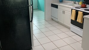 Een keuken met witte kastjes, een zwarte koelkast, een fornuis en een spoelbak.