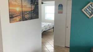 Een gang met een bed, een plafondventilator en een deur naar een andere kamer.