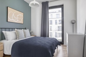 Un dormitorio moderno con cama, mesita de noche, cómoda, un cuadro, ventana con cortinas y vistas al balcón.