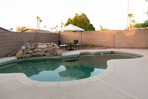 Enjoy a backyard retreat with a swimming pool, patio, and outdoor seating area surrounded by lush palm trees.