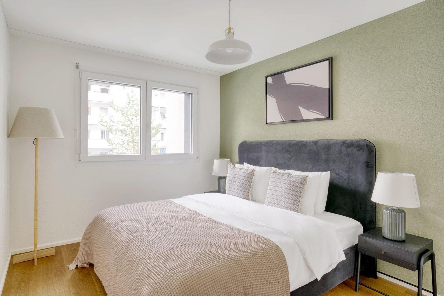 Ein Schlafzimmer mit einem Bett, zwei Nachttischen, einer Stehlampe, einem Fenster und einem Bild an der Wand.