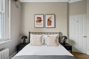 A bedroom with a bed, two bedside tables, a radiator, and a door. - Sunlit Bayswater 2BR w/ High Ceilings, near Hyde Park, by Blueground (London)