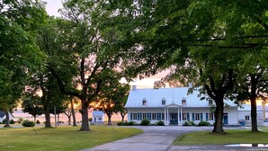 A large white building with a symmetrical facade, a central entrance with columns, and a surrounding lawn with mature trees. - Cottage - The Retro   (Saint-Michel-de-Bellechasse)