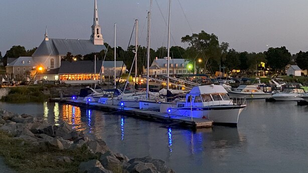 A marina with boats docked, a church with a steeple, and a building with lights on. - Cottage - The Retro   (Saint-Michel-de-Bellechasse)