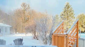A hot tub with a wooden deck and stairs leading up to it, surrounded by snow-covered trees and a house in the background. - Cottage - The Retro   (Saint-Michel-de-Bellechasse)