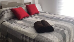 A neatly made bed with a checkered bedspread, two red pillows, and two rolled towels. - SPA BEACH HOUSE con PLAYA PRIVADA/PISCINA/JACUZZI (Manta)