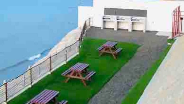 A coastal view with a grassy area, picnic tables, and a white building with a red gate. - SPA BEACH HOUSE con PLAYA PRIVADA/PISCINA/JACUZZI (Manta)