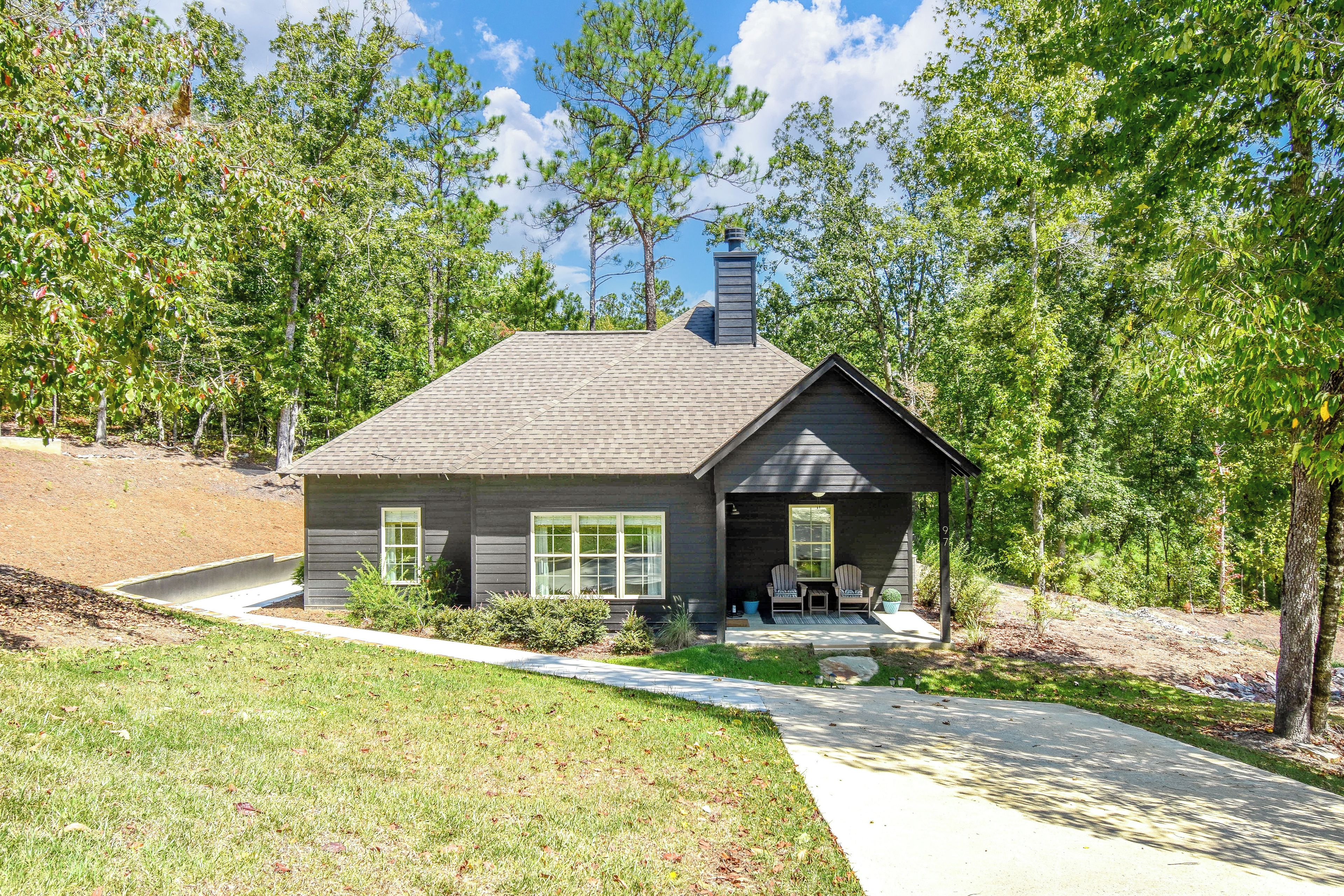 A single-story house with a dark gray exterior, a chimney, and a covered porch with two chairs.