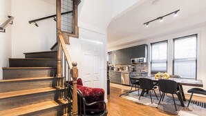 A staircase with wooden steps and a handrail, a dining area with a table and chairs, and a kitchen with cabinets and appliances. - Charming & Comfy Gem ~ 10 Mins to Downtown ~Patio! (Chicago)