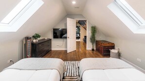 A bedroom with two beds, a dresser, a radiator, a television, and a door leading to a bathroom. - Charming & Comfy Gem ~ 10 Mins to Downtown ~Patio! (Chicago)
