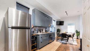 A modern kitchen with a stainless steel refrigerator, grey cabinets, a built-in oven, and a dining area with a table and chairs. - Charming & Comfy Gem ~ 10 Mins to Downtown ~Patio! (Chicago)