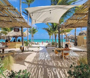 Un restaurante frente a la playa con terraza, palmeras y vistas al océano.