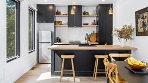 Een moderne keuken met donkere kastjes, een centraal keukenblok met krukken, een koelkast en een spoelbak.