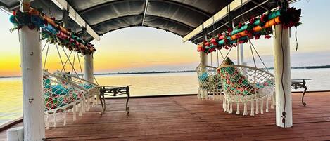 Una terraza de madera con área techada, hamacas y una mesa.