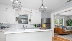Una cocina moderna con armarios blancos, una isla central, un refrigerador de acero inoxidable y dos lámparas colgantes.