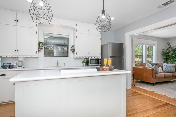 Una cocina moderna con armarios blancos, una isla central, un refrigerador de acero inoxidable y dos lámparas colgantes.