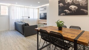 Un salon moderne comprenant un canapé, une table à manger et des chaises, un téléviseur et une œuvre d’art représentant des méduses, accrochée au mur.