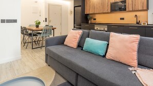 Un salon moderne avec un canapé gris, une table à manger avec des chaises et un coin cuisine doté de meubles en bois et d’un four à micro-ondes.