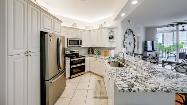 Una cocina moderna con armarios blancos, electrodomésticos de acero inoxidable, un ventanal y un balcón con mobiliario exterior.