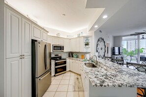 A modern kitchen with white cabinetry, stainless appliances, a large window, and a balcony with outdoor furniture. - Naples Escape in Regatta w/ Resort Amenities! (Naples)