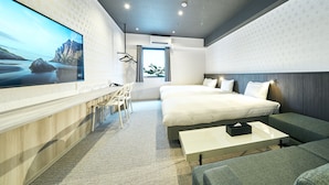 A modern hotel room with a large flat-screen TV, a desk with chairs, a bed with two pillows, a bedside table, and a sofa. - Rakuten STAY Kokura Station (Kitakyushu)