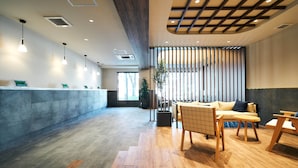 A modern reception area with a wooden floor, a reception desk, and seating area with wooden chairs and a sofa. - Rakuten STAY Kokura Station (Kitakyushu)