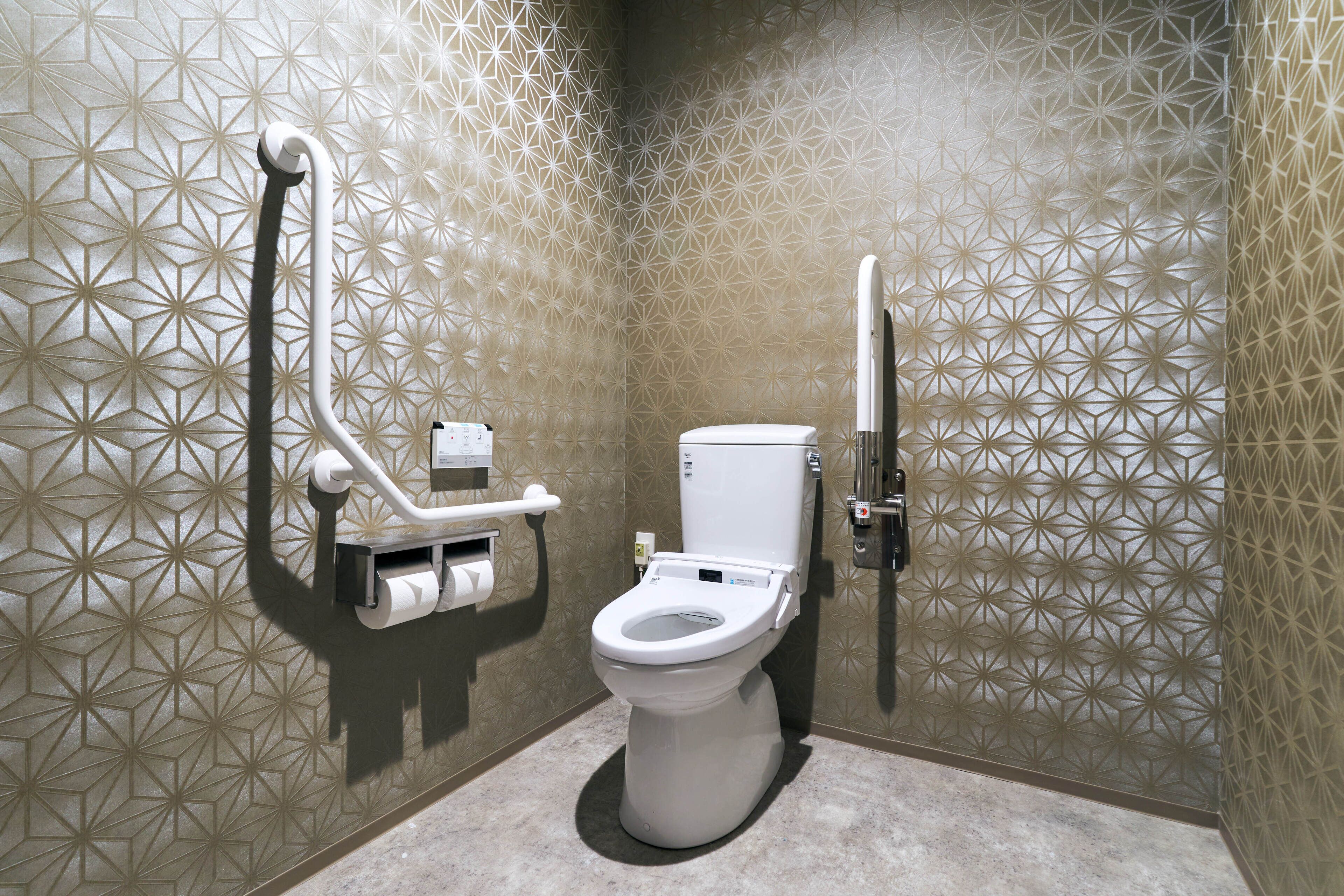 A modern bathroom with a geometric patterned wall, a toilet, and a hand dryer.