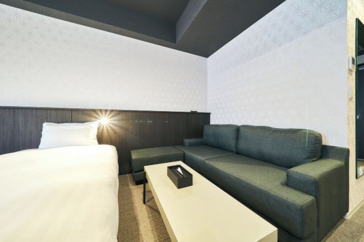 A modern hotel room with a bed, a sofa, a coffee table, and a nightstand.