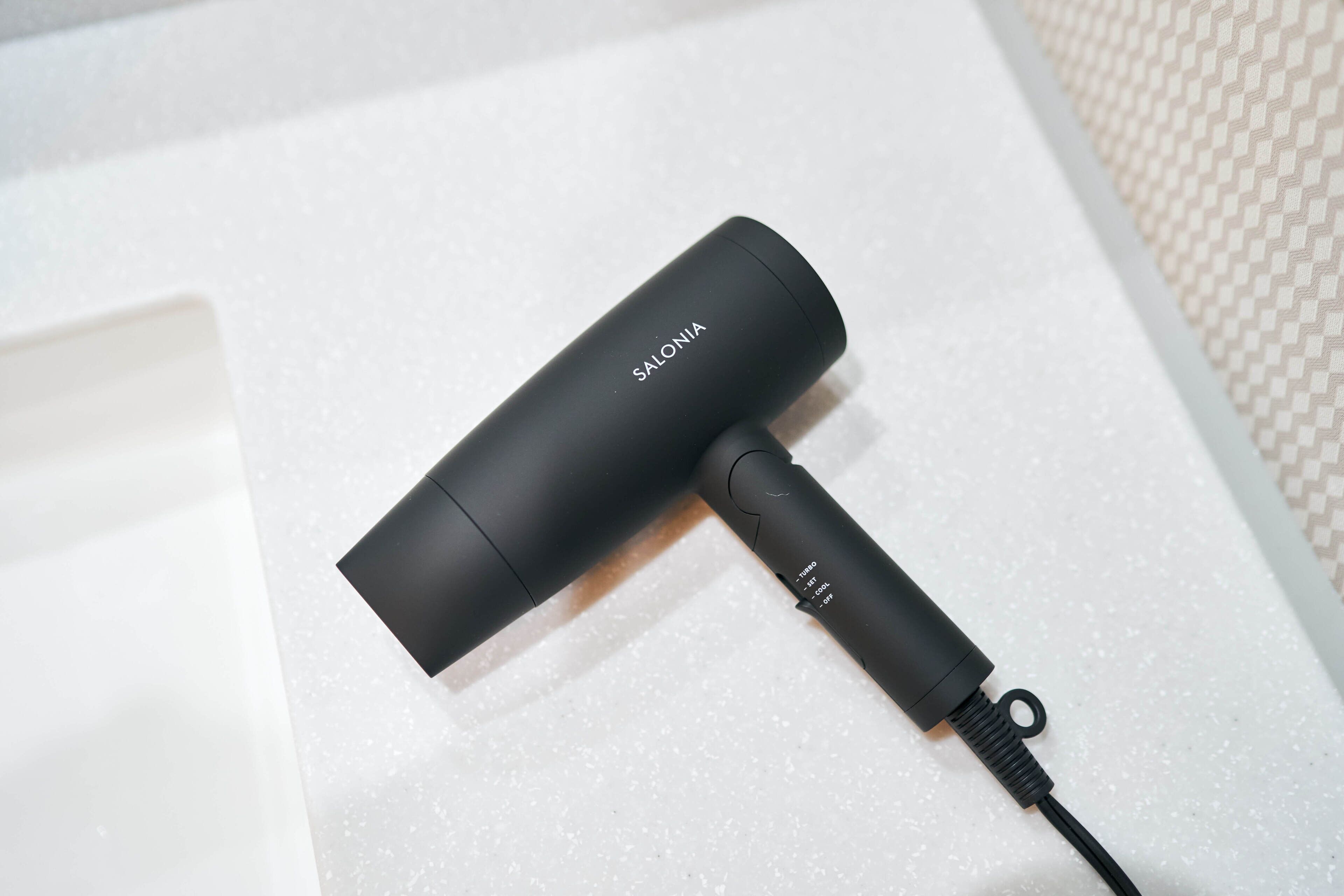 A black portable charger with the brand name 'SALONIA' on it, lying on a white textured surface.