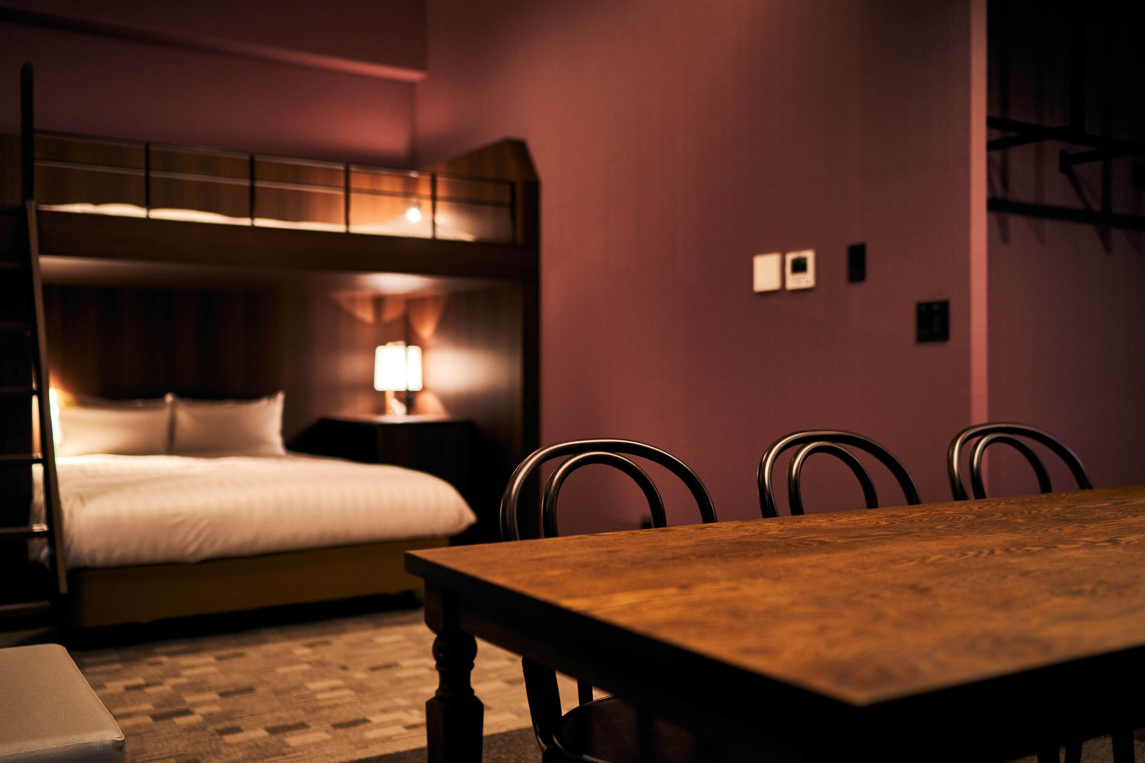 A hotel room with a bunk bed, a wooden dining table, and four chairs.