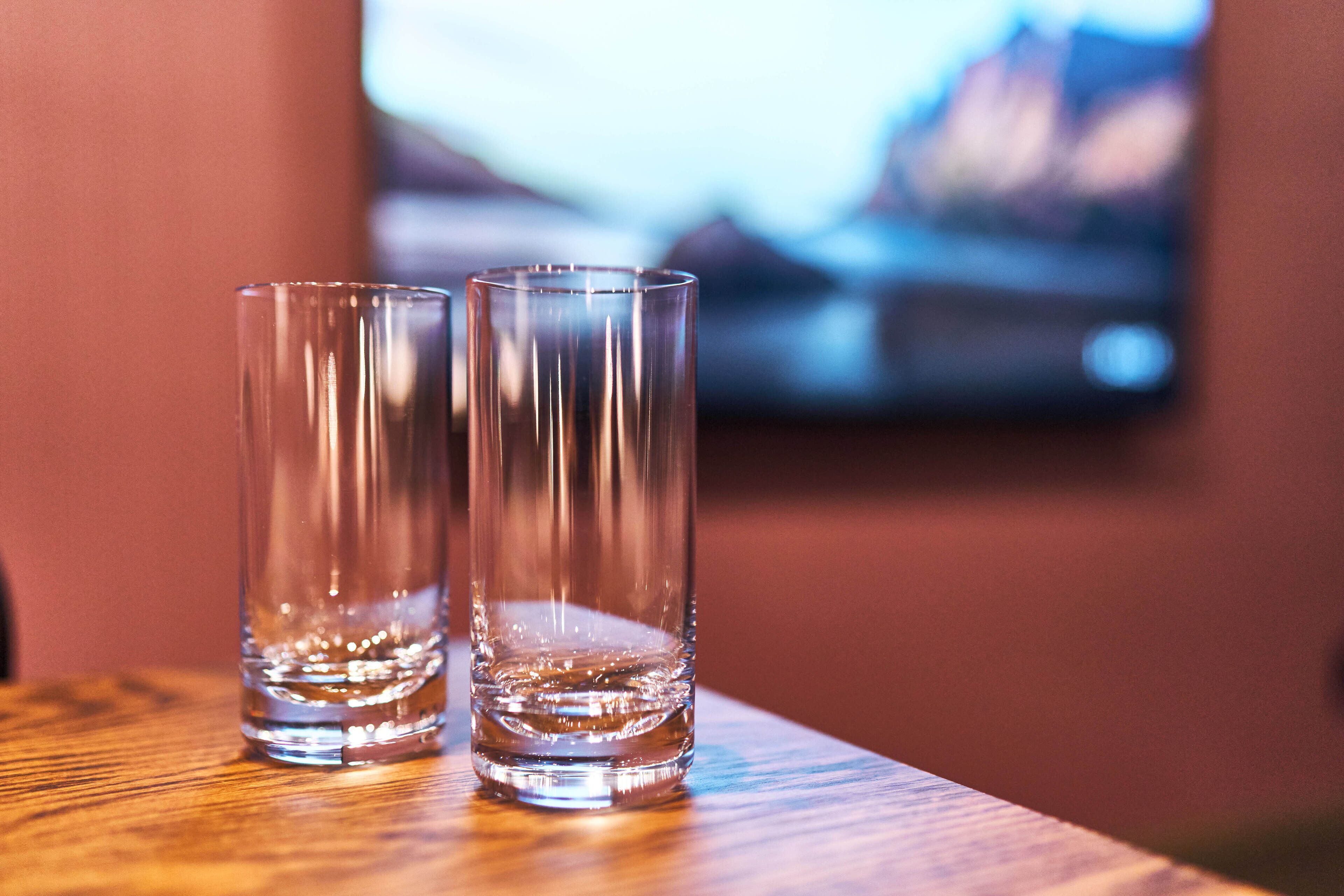 Two clear glasses on a wooden surface with a blurred background.
