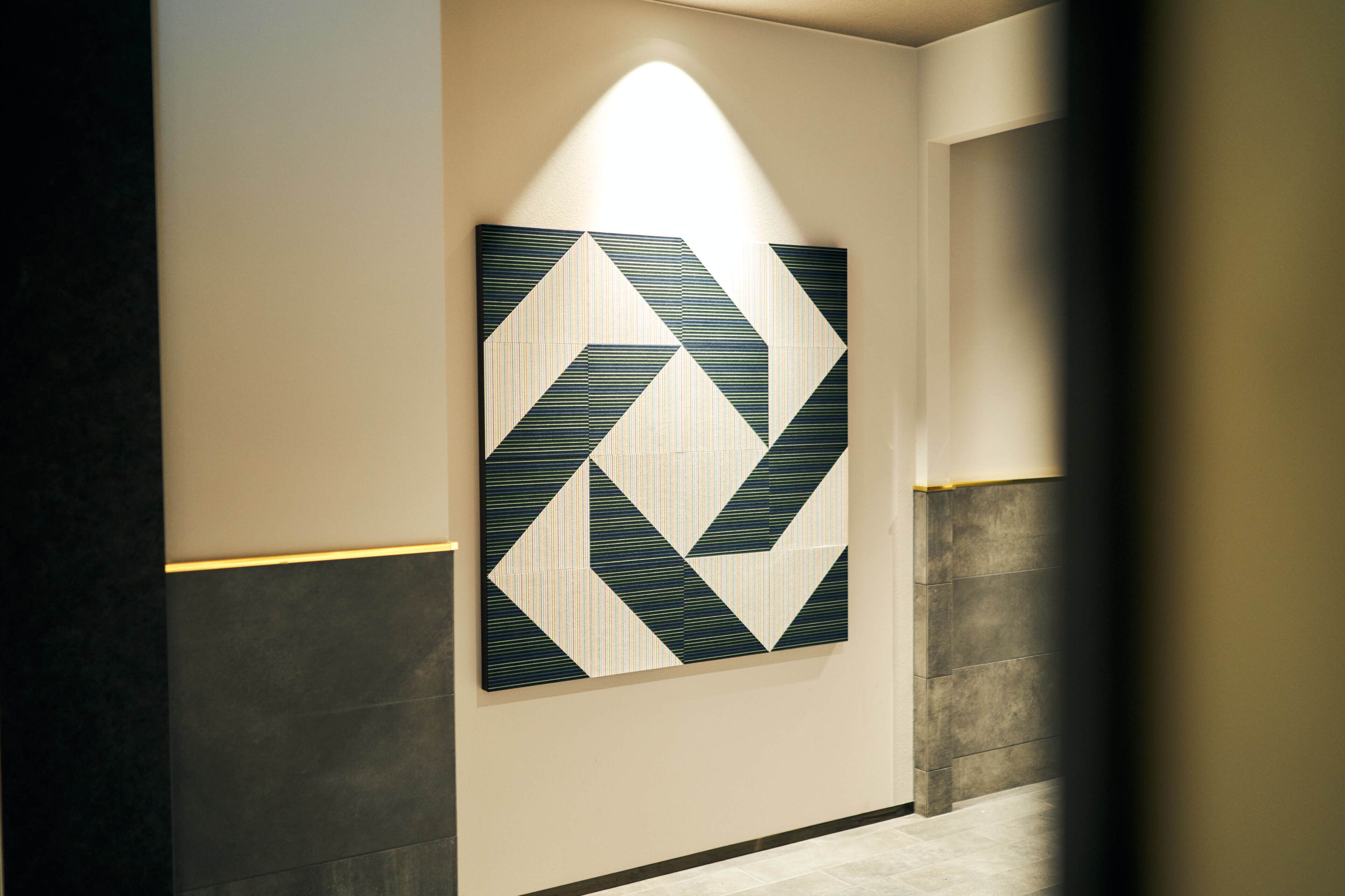 A hallway with a geometric wall art piece and a tiled floor.