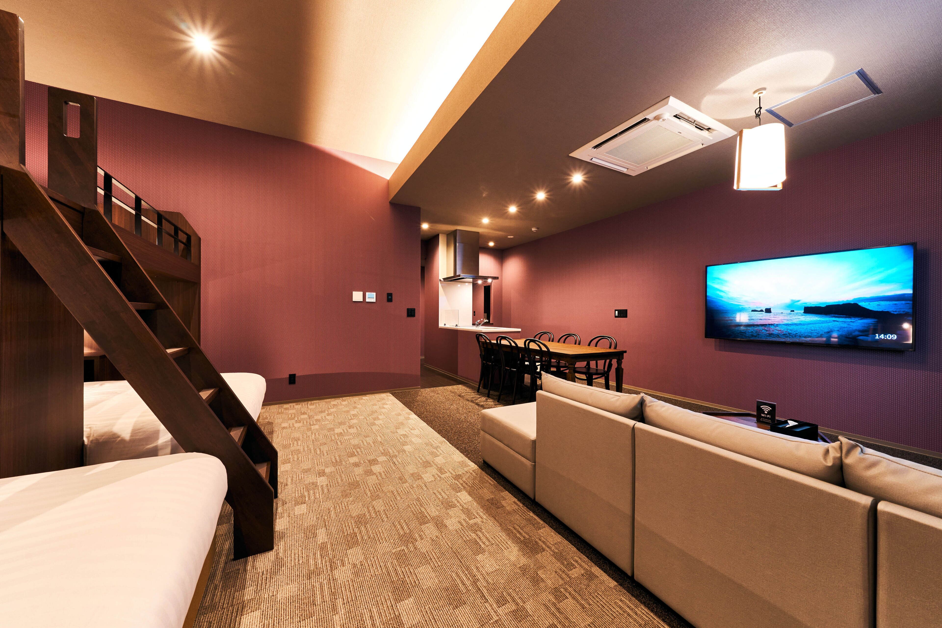 Habitación de hotel con televisor grande, sofá, mesa de comedor y una escalera.