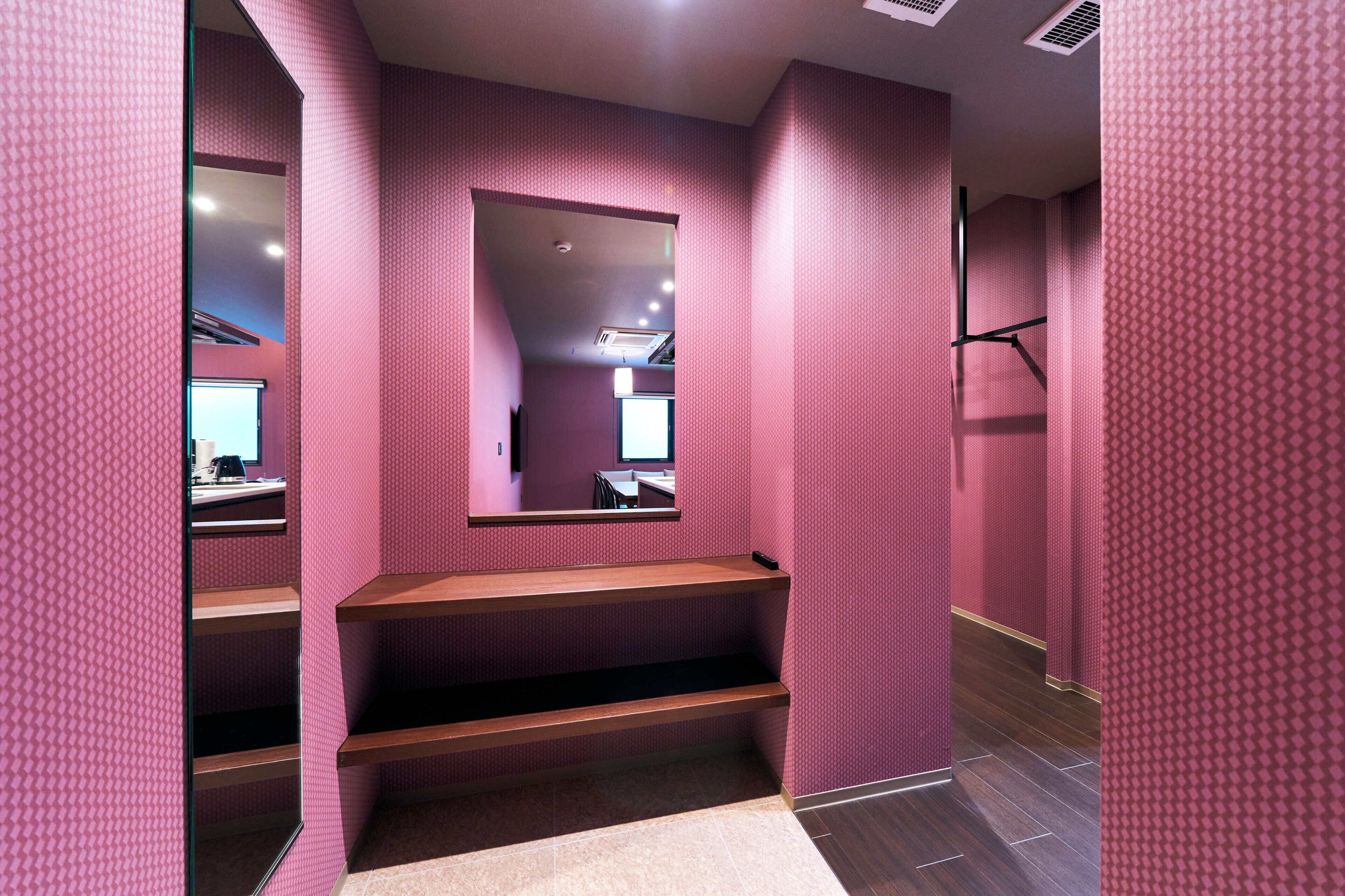 A hallway with pink patterned walls, a wooden bench, and a mirror on the left.