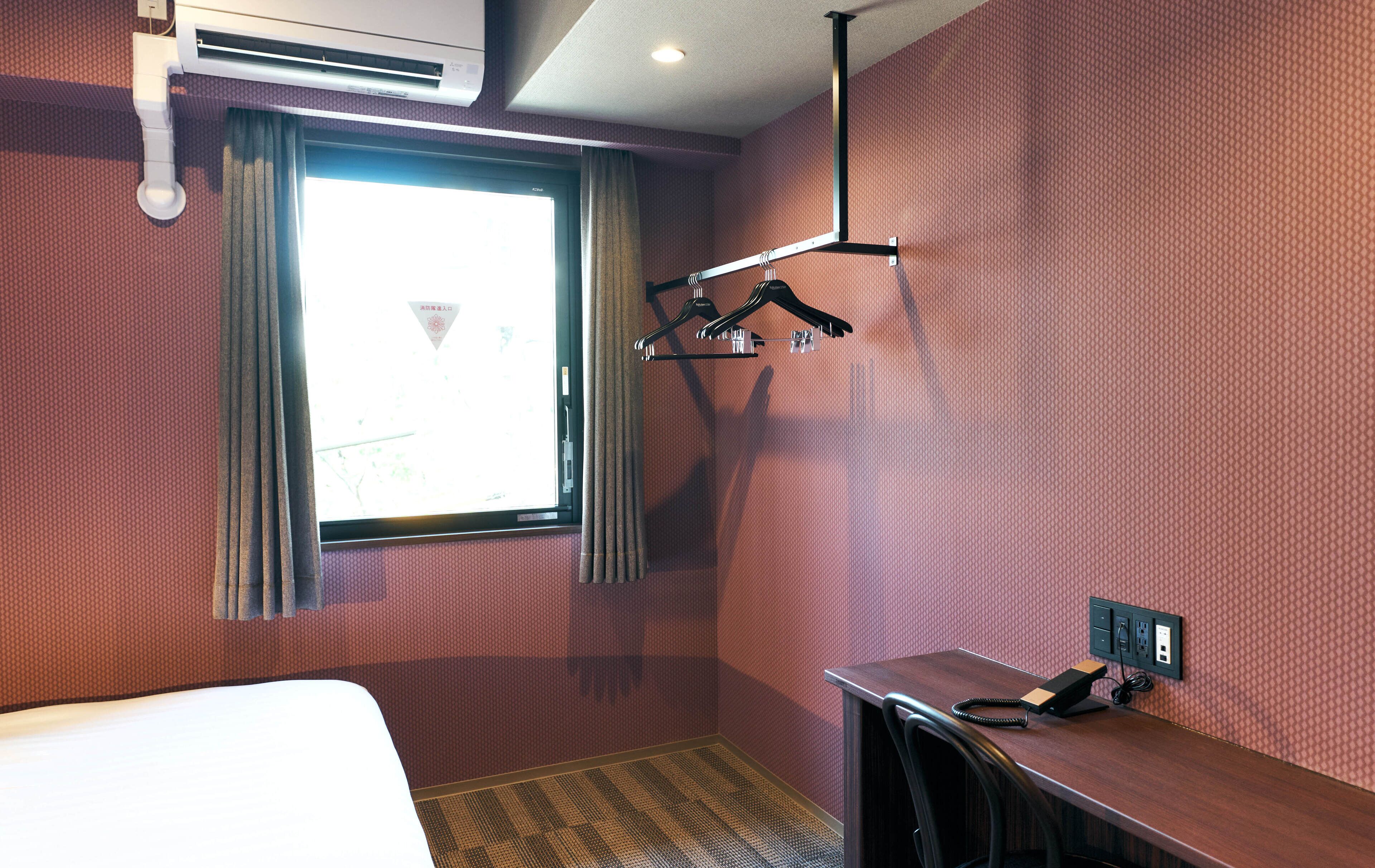 Una habitación de hotel con cama, escritorio, teléfono y ventana con cortinas.