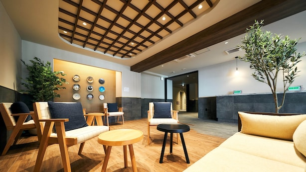 A modern lobby with wooden furniture, a large plant, and a wall with circular designs. - Rakuten STAY Kokura Station (Kitakyushu)