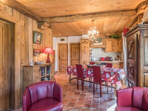 Een rustiek houten interieur met een eethoek, rode leren stoelen, een kroonluchter en houten kasten.