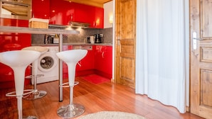 A modern kitchen with red cabinets, stainless steel appliances, and two white bar stools. - Appartement du Poutat - Welkeys (Huez)