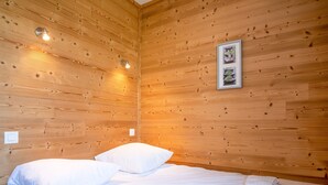 A wooden-paneled room with a bed, pillows, a framed picture, and a light fixture. - Appartement du Poutat - Welkeys (Huez)
