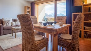 A cozy living room with a wooden dining table, wicker chairs, a sofa, and a bookshelf. - Appartement du Poutat - Welkeys (Huez)