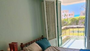 Een kamer met twee bedden, een nachtkastje en een raam met uitzicht op gebouwen en groen.