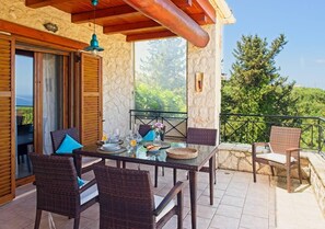 A dining area with wicker furniture, a glass table, and a stone wall backdrop. - Villa Petalouda Stunning Villa in Tragaki Zante (Tragaki, zakynthos)