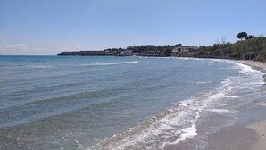Una playa con agua cristalina, una orilla de arena y edificios al fondo.