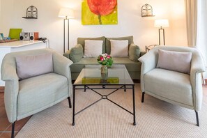 A living room with two armchairs, a sofa, a glass coffee table, and a painting on the wall.